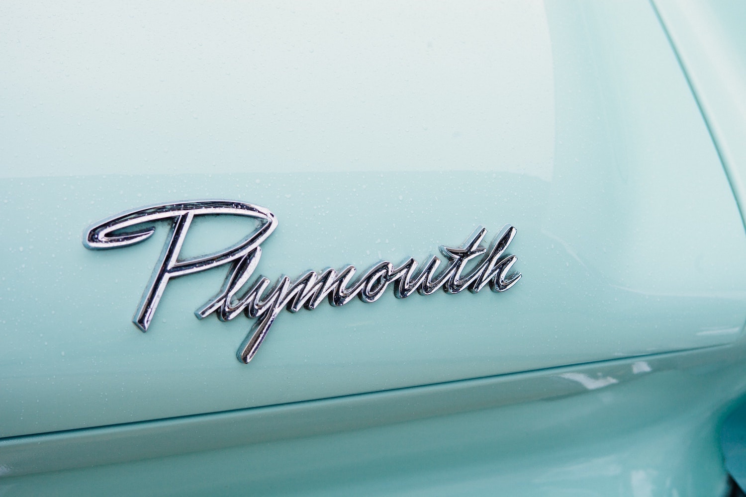 Chrome Plymouth brand logo on the trunk of an aqua-colored classic car.