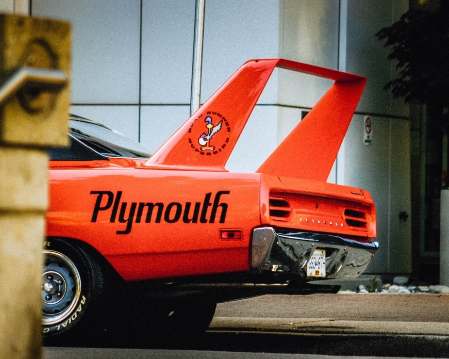 The "Plymouth" brand printed on the rear fender of a bright orange Superbird muscle car.