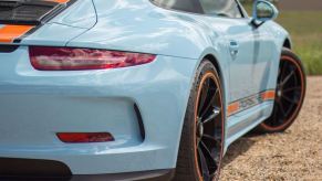 The rear fender of a powder blue porsche wearing the marigold orange stripes of Gulf Oil racing liveries as a tribute to the 917 that ran at Le Mans.