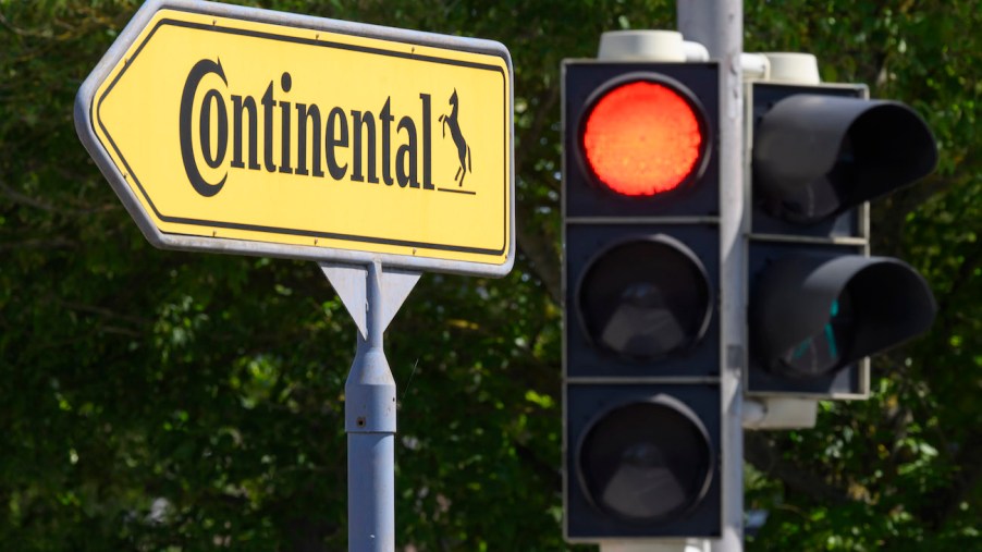 A red traffic light on a traffic light shines next to a sign pointing the way to the Continental plant.