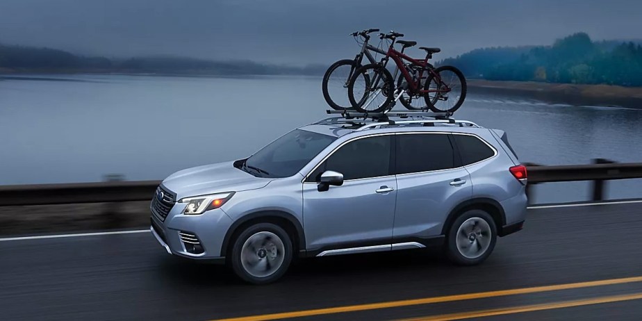 A blue 2023 Subaru Forester small SUV is driving on the road. 
