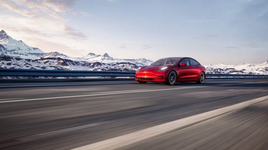 A red Tesla Model 3 Performance blasts down a mountain road in the snow.