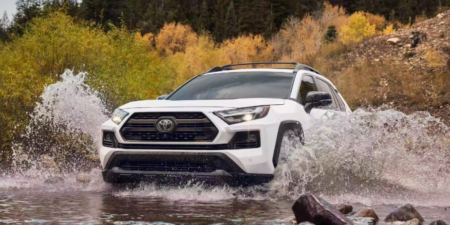 A white 2023 Toyota RAV4 small SUV is driving through a puddle.