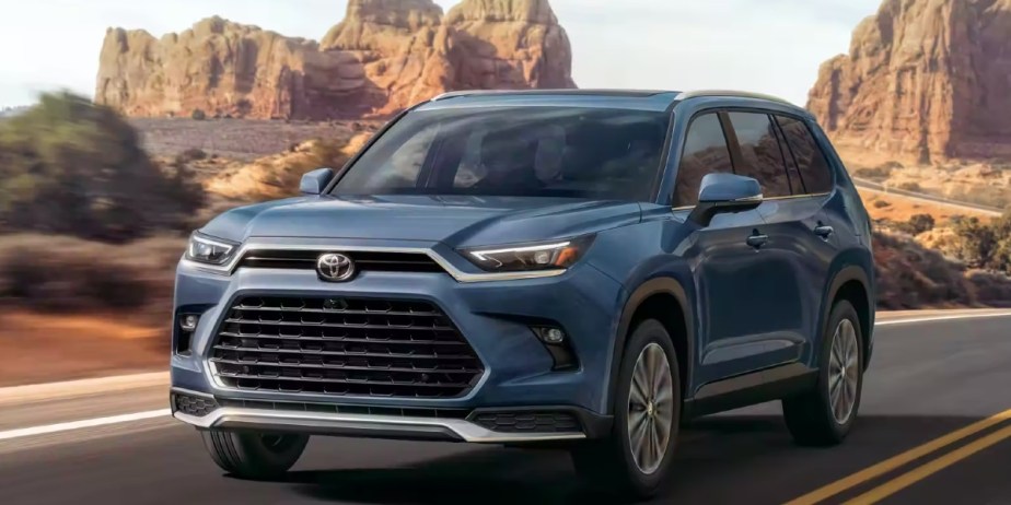 A blue 2023 Toyota Grand Highlander midsize SUV is driving on the road. 