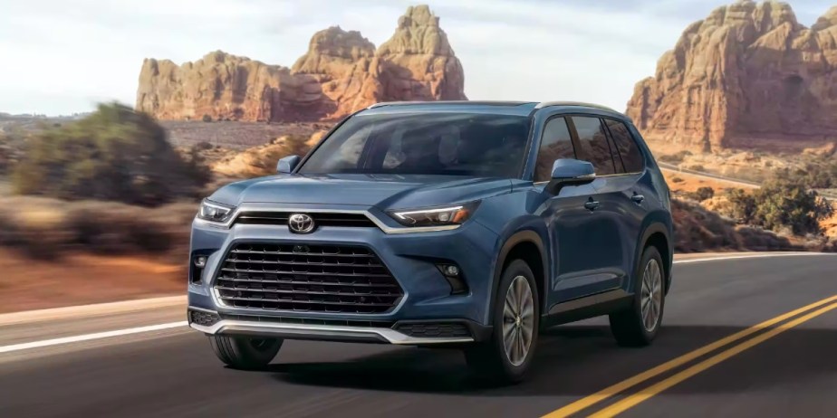 A blue 2024 Toyota Grand Highlander midsize SUV is driving on the road.