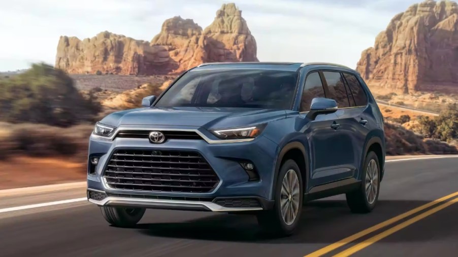 A blue 2024 Toyota Grand Highlander three-row midsize SUV is driving on the road.