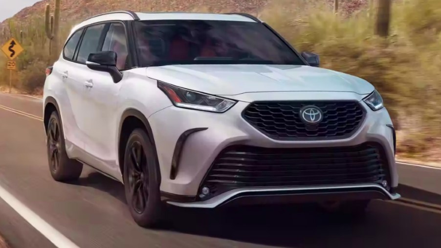 A white 2023 Toyota Highlander midsize SUV is driving on the road.