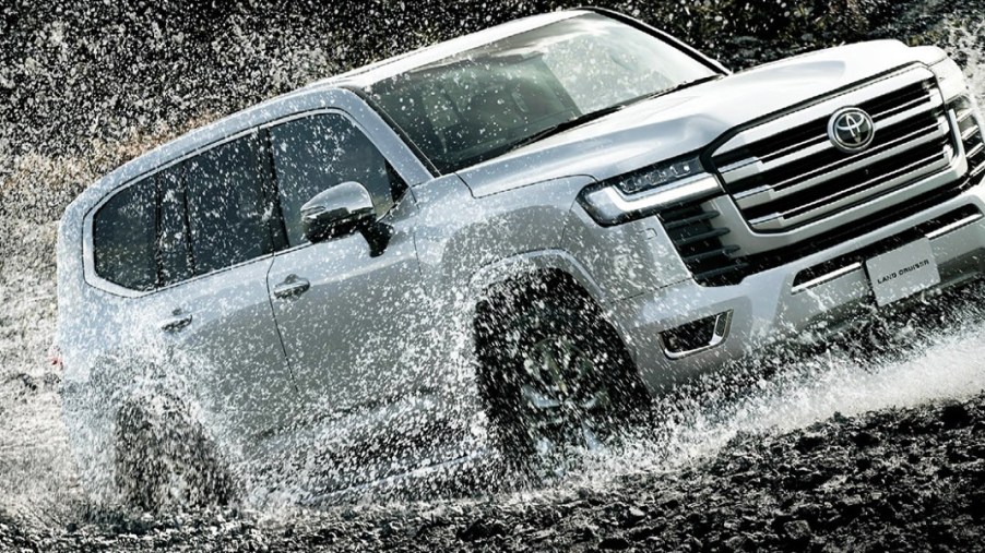 A gray Toyota Land Cruiser full-size SUV is driving through the water.