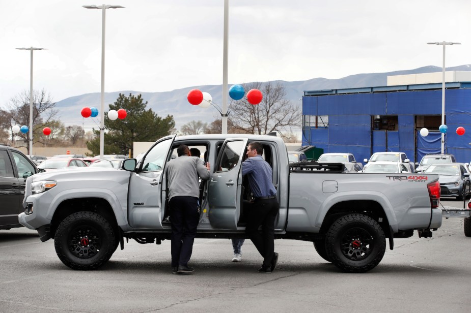 A salesperson shows customers a popular midsize Toyota Tacoma pickup truck, all four of its doors open in a dealership parking lot.