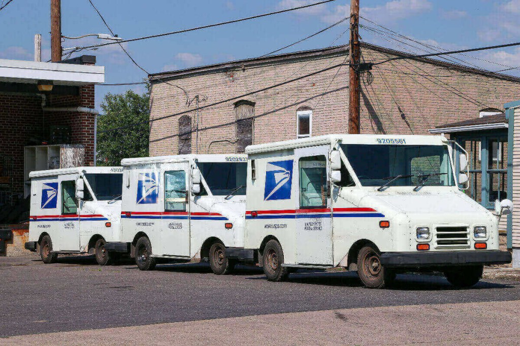 A group of Grumman LLV USPS mail trucks is parked.