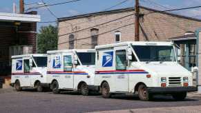 A group of Grumman LLV USPS mail trucks is parked.