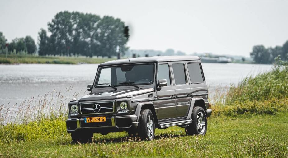 Used Mercedes-Benz G Wagon SUV parked on a grassy field, a river and tree-line visible in the background.