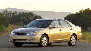 A gold used Toyota Camry shows off its sedan side profile and reflective paint.