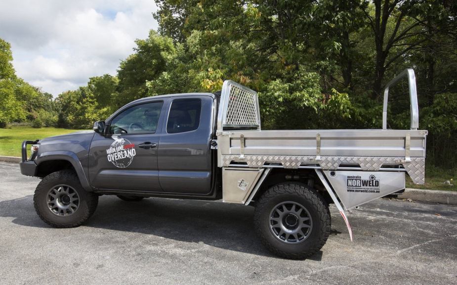 A versatile utility or Ute pickup truck bed on a truck parked in a lot, trees visible in the background.