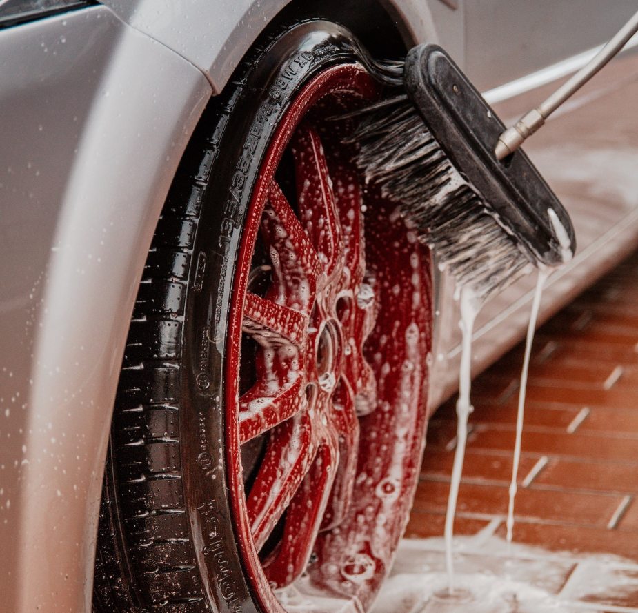 Closeup of a scrub brush cleaning mud or ice off a soapy red sports car rim.