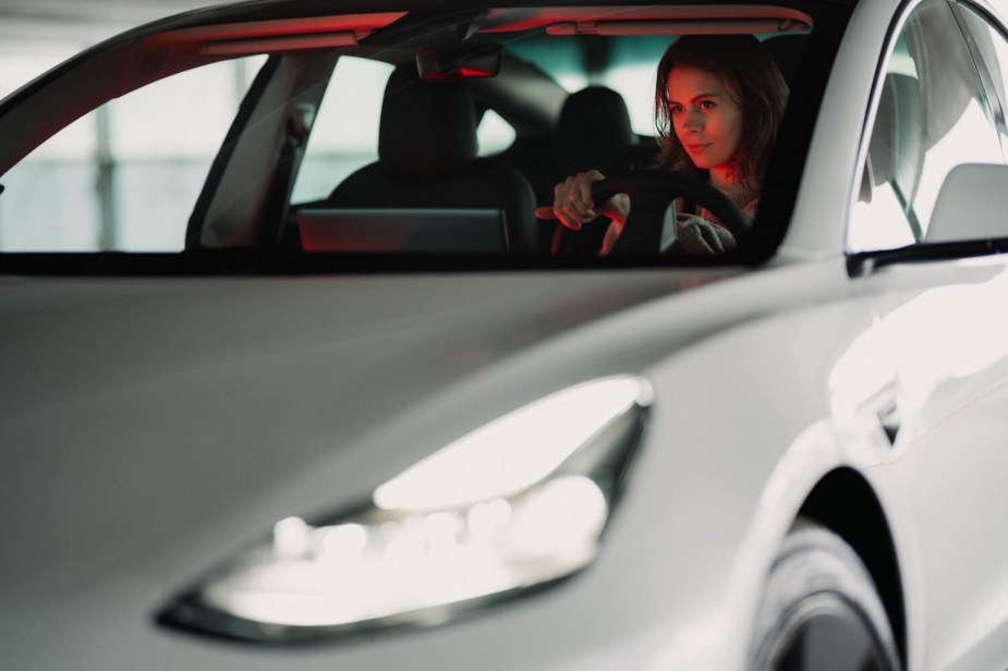 A female driver looking over the wheel of her Tesla EV may pay more for car insurance based on her Tesla.