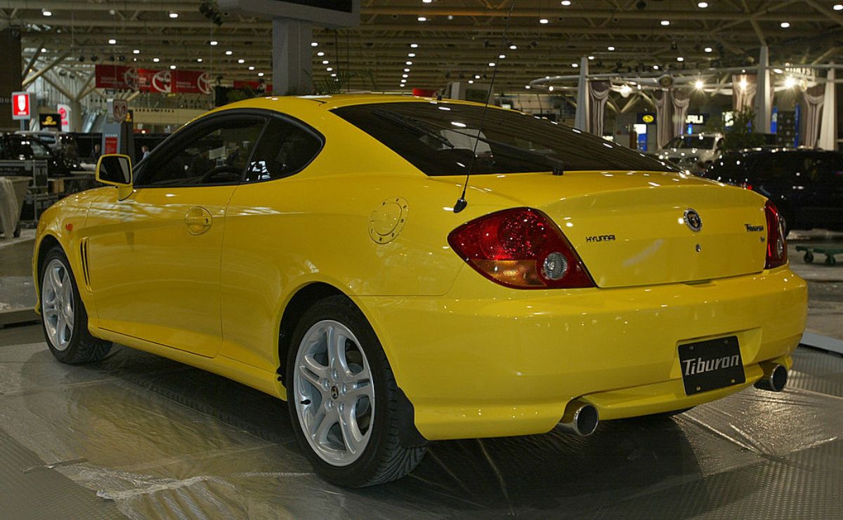 A yellow 2003 Hyundai Tiburon on display at an auto show.