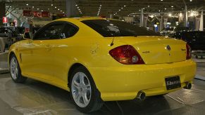 A yellow 2003 Hyundai Tiburon on display at an auto show.