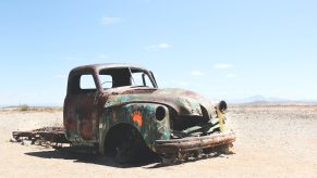 The remains of a classic pickup truck rust in the desert, sand and mountains visible in the background.