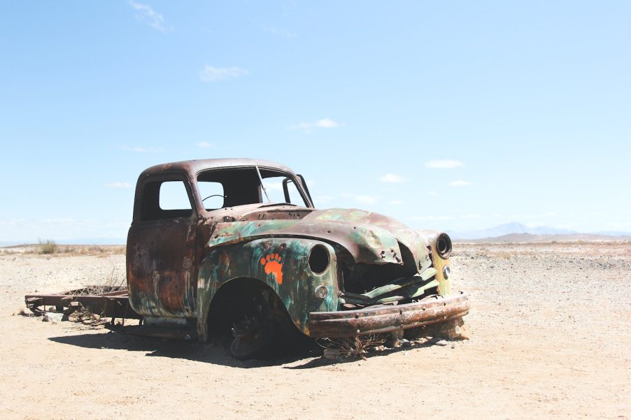 The remains of a classic pickup truck rust in the desert, sand and mountains visible in the background.