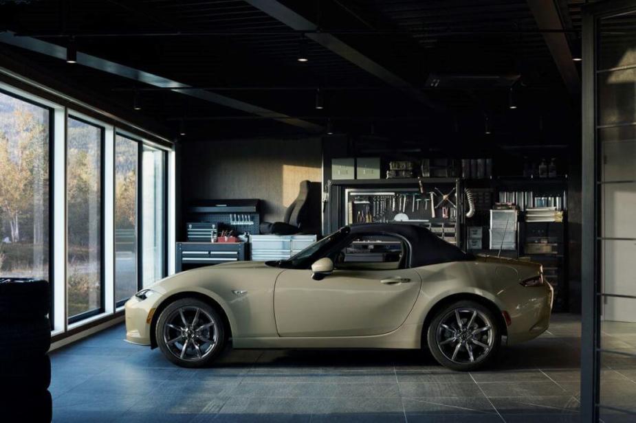 A side profile shot of a beige 2023 Mazda MX-5 Miata convertible roadster model parked inside a garage
