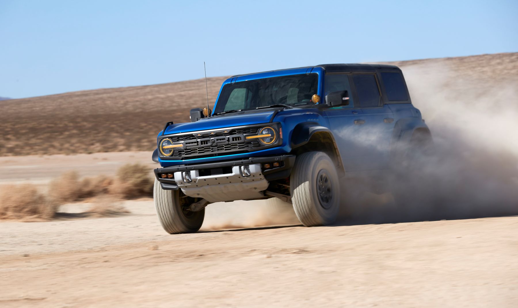 A blue 2022 Ford Bronco Raptor undergoing off-road driving training through dirt and sand