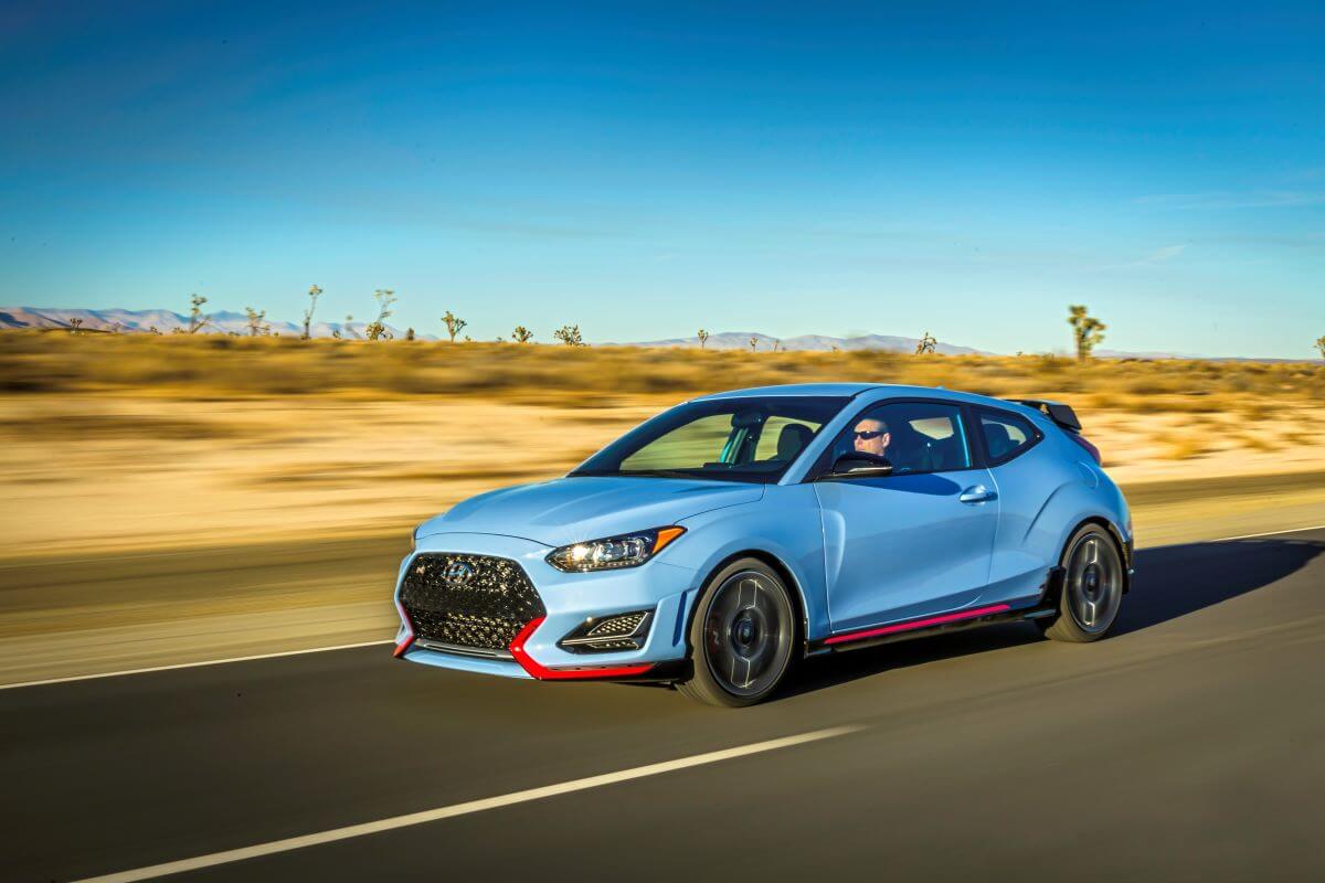 A light blue with red trimming 2022 Hyundai Veloster N performance hatchback model driving down a desert highway