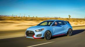 A light blue with red trimming 2022 Hyundai Veloster N performance hatchback model driving down a desert highway