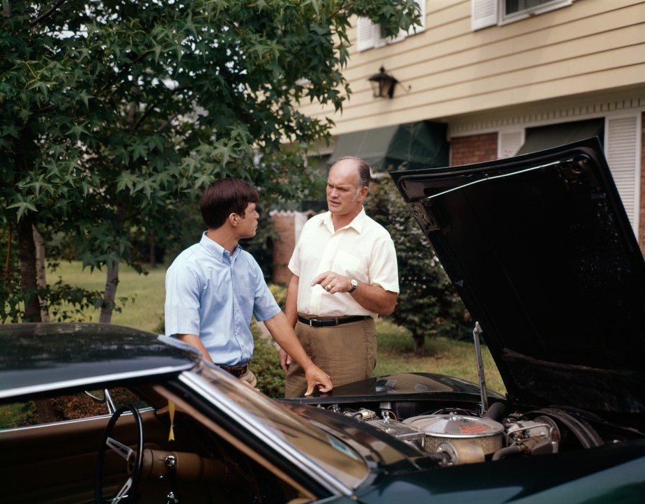 A young and old man inspect a classic car together.
