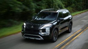 A black 2023 Mitsubishi Outlander PHEV plug-in hybrid compact SUV model driving on a forest highway