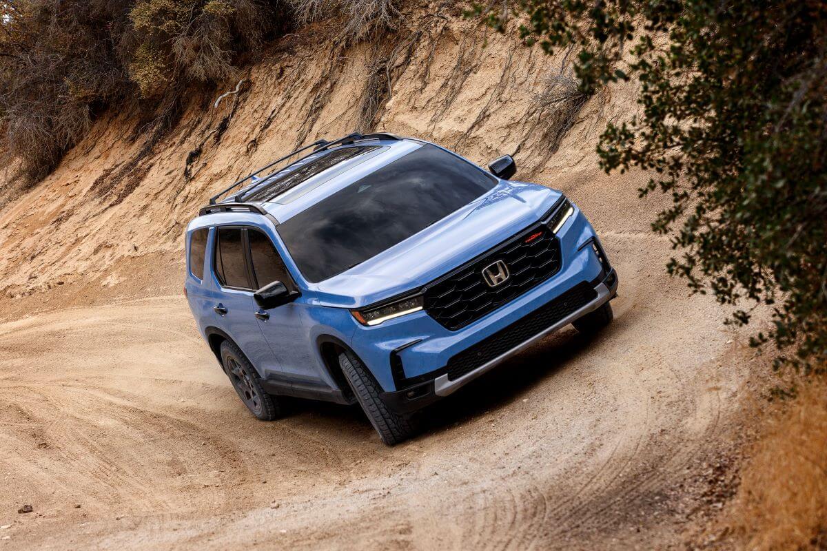 A light blue 2023 Honda Pilot TrailSport midsize crossover SUV model driving off-road on dirt trails