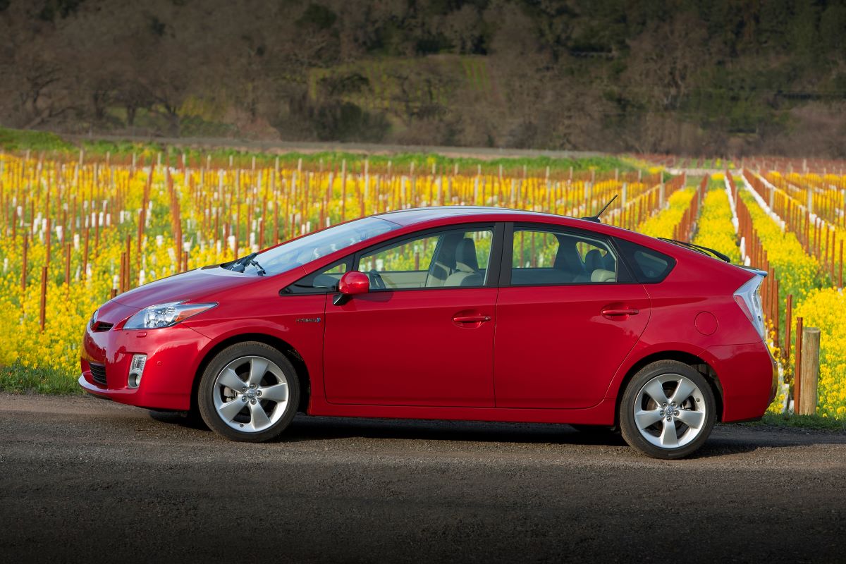 A red 2010 Toyota Prius hybrid hatchback model parked near a field of yellow flowers