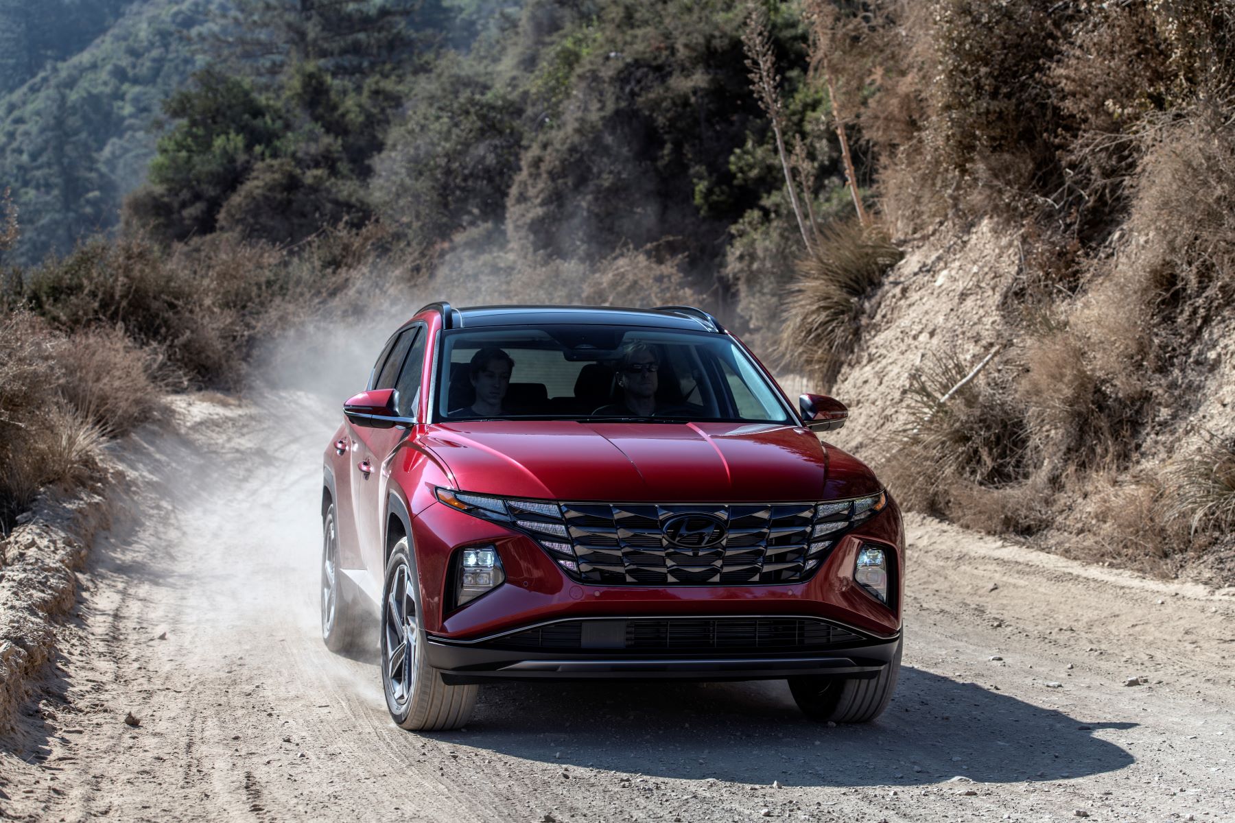 A red 2023 Hyundai Tucson compact SUV model driving on a dirt road as its tires kick up dust