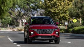 A red 2023 Hyundai Tucson compact SUV model driving in the suburbs near a crosswalk