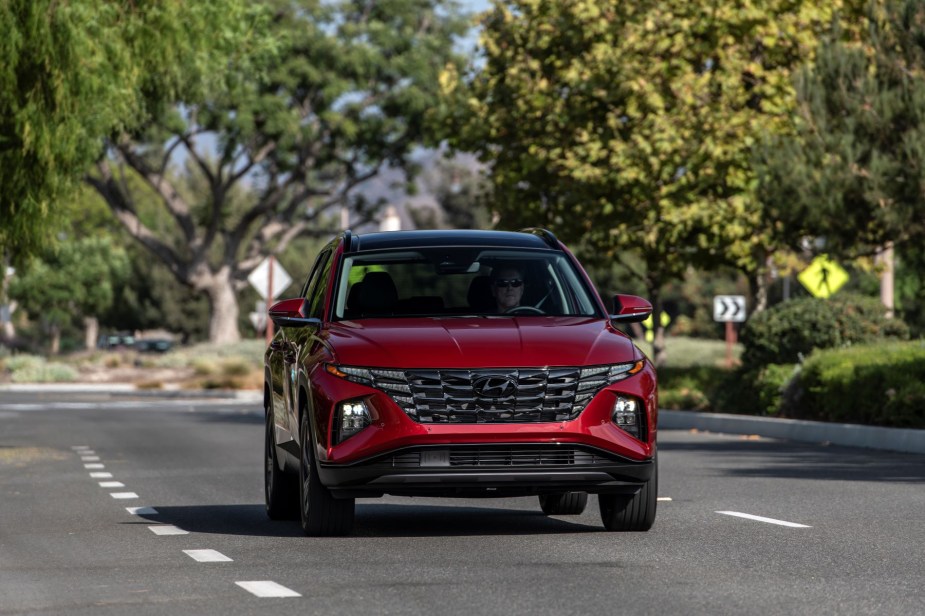 A red 2023 Hyundai Tucson compact SUV model driving in the suburbs near a crosswalk