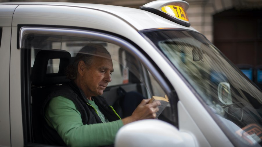Cab driver reads a book in his car