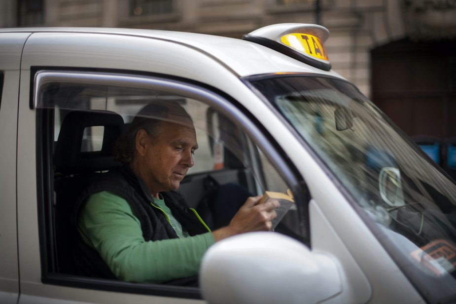 Cab driver reads a book in his car