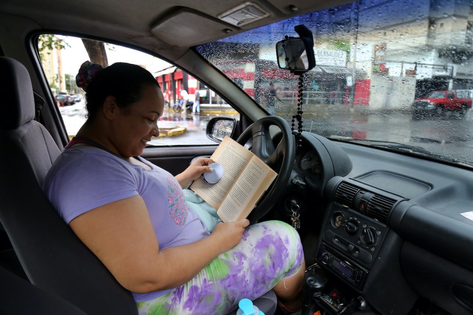 A woman reads a book in her car.