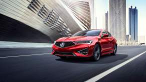 A red Acura ILX driving down a road within a city.