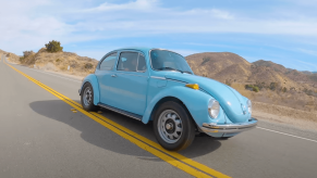 Blue 1973 Volkswagen Beetle racing along a remote road in California, desert ridgelines visible in the background.