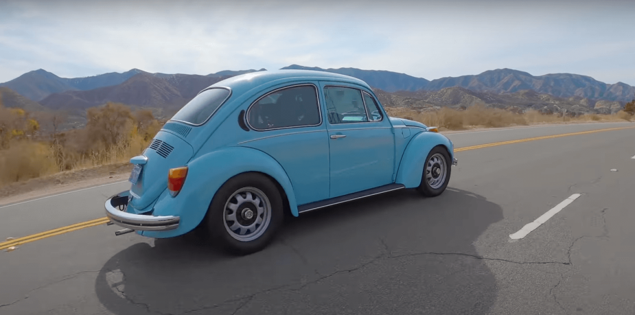The back of a blue 1974 VW Super Beetle bug driving down the highway.