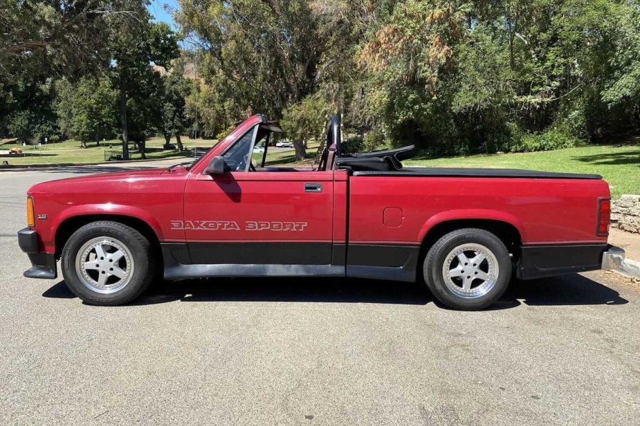 Profile photo of a Dodge Dakota sport convertible pickup truck parked in front of a row of trees and a city park.