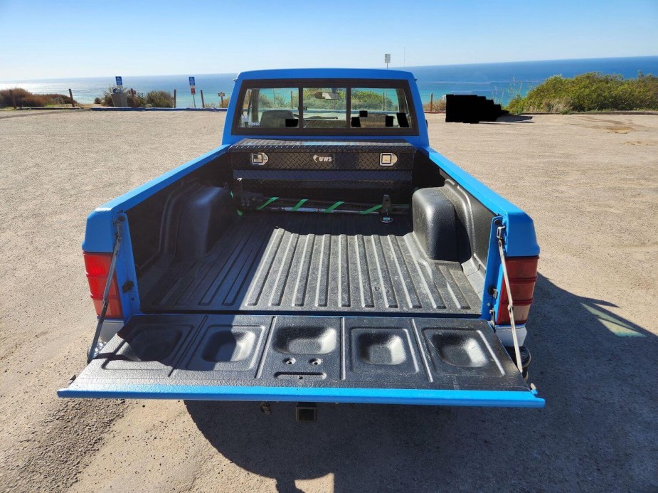 The bed of a blue 1990 Jeep Comanche 4x4 pickup truck, with the ocean visible in the distance.