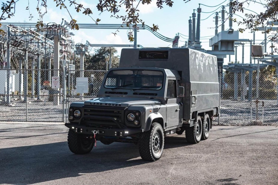 Promo photo of a Land Rover Defender 6x6 truck up for auction, a power station visible in the background.