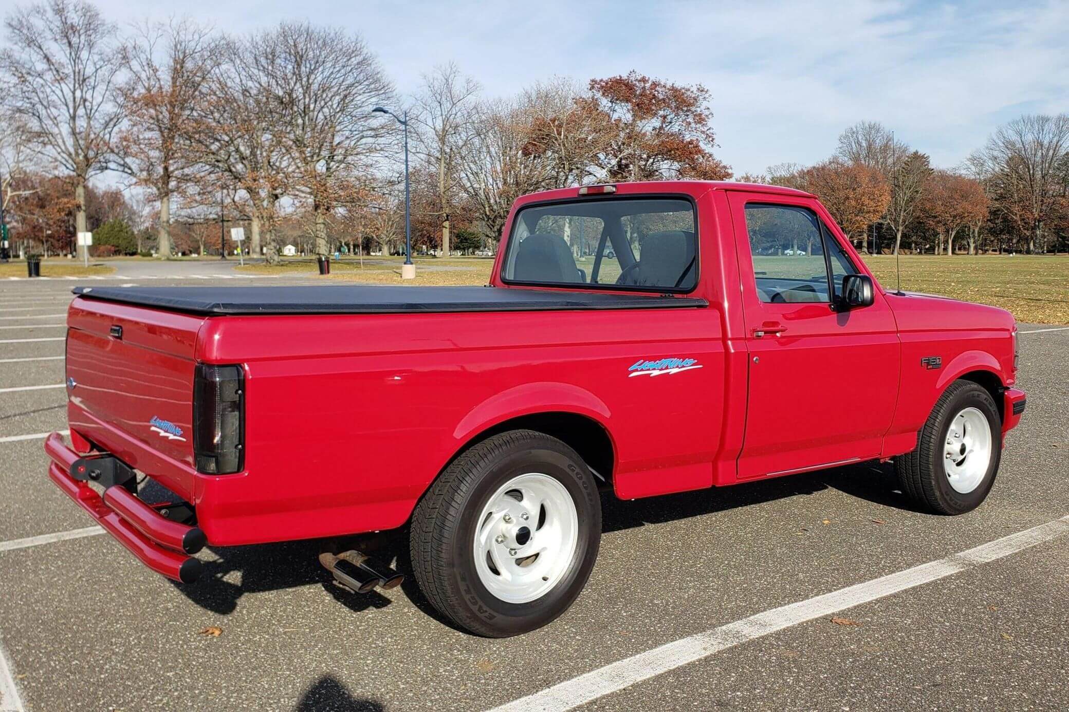 Red Ford F-150 Lightning used supertruck in a parking lot, trees visible in the background.