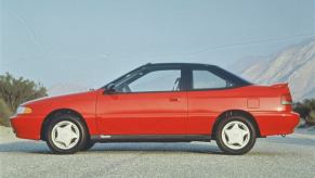 A side profile shot of a red 1994 Hyundai Scoupe model parked near foggy mountains