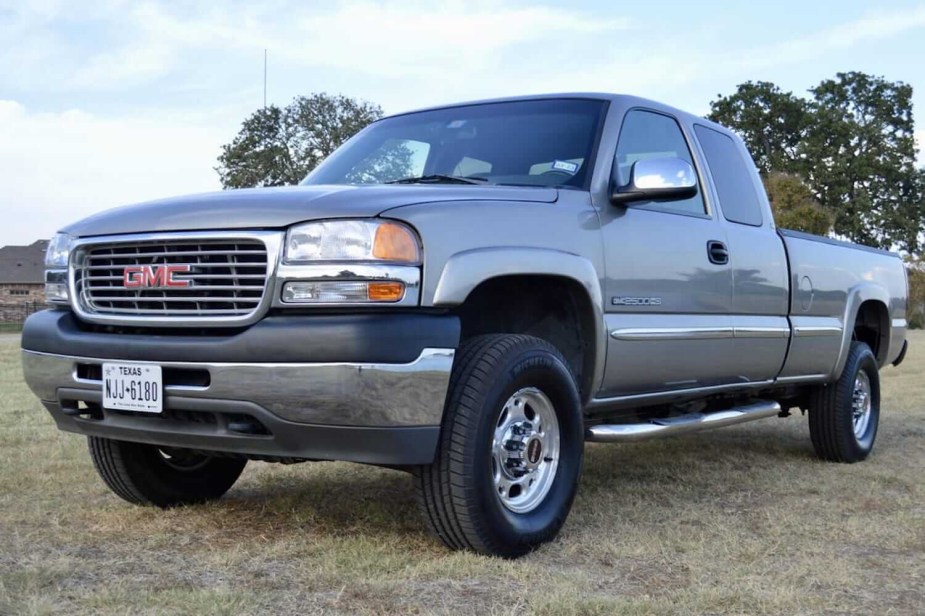 A beige/silver 2002 GMC Sierra GMT800 pickup truck with an extended cab parked in a field for an auction photo.