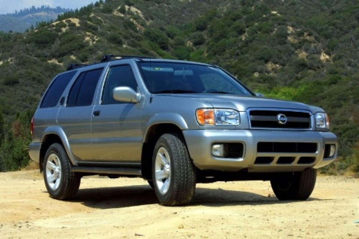 A silver-gray 2003 Nissan Pathfinder midsize SUV model parked on a dirt plain in a mountain forest