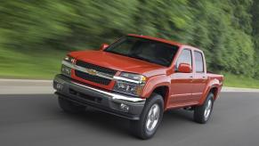 An orange 2009 Chevrolet Colorado (first-generation) driving towards the camera fro a promo photo, trees visible in the background.