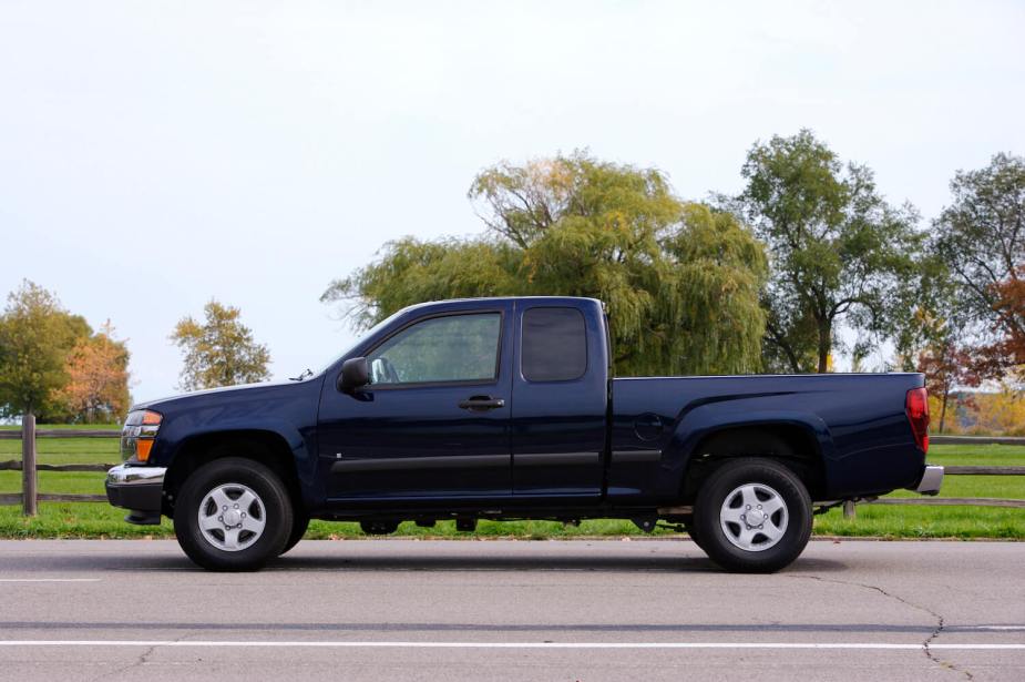 Profile view of a GMC Canyon compact pickup truck parked in front of a fence and trees.